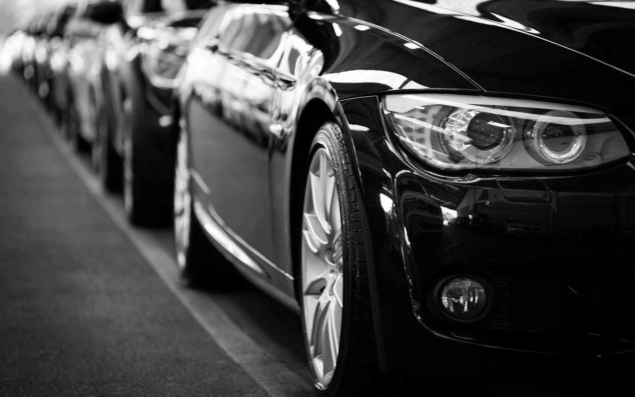 about-us Close-up black and white image of a luxury car line-up focusing on vehicle headlights.